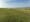 Wide expanse of flat green grass leading to distant sea with silhouettes of people in the distance